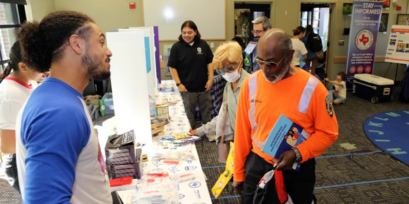photo of young male talking to older male at an informational booth at a public educational event for emergency preparedness.