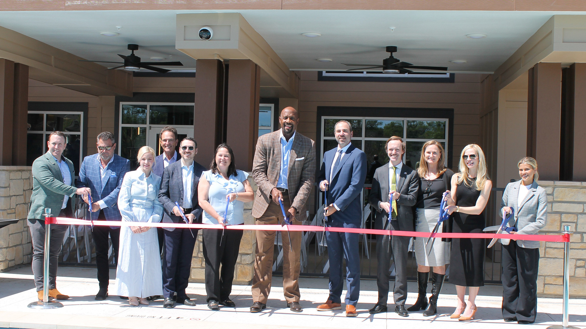 Rendering shows 12 individuals, eight of which are holding scissors, poised to but a red ribbon that is stretched in front of them.