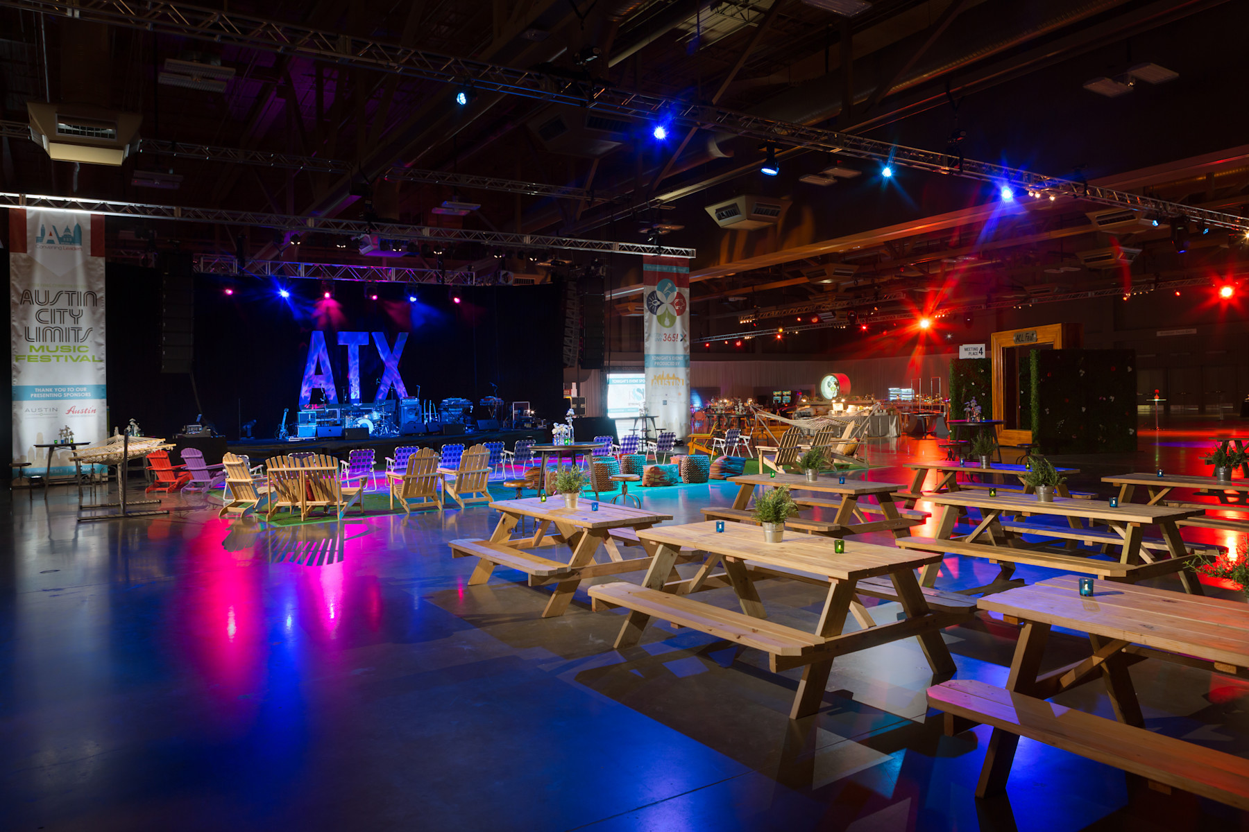 Image of a Palmer Events Center exhibit hall set up for a corporate party with picnic tables, chairs, and an ATX sign with lights