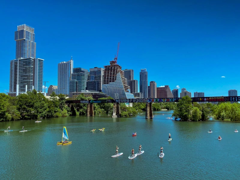 photo of Downtown Austin skyline on sunny day with multiple people on paddleboards and kayaks on Lady Bird Lake.