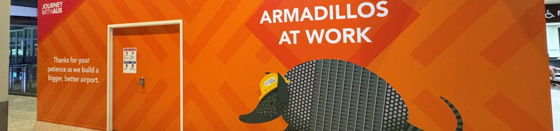 Construction sign at the airport with an armadillo in a construction hat and the words Armadillos at Work - Thanks for your patience as we build a bigger, better airport.