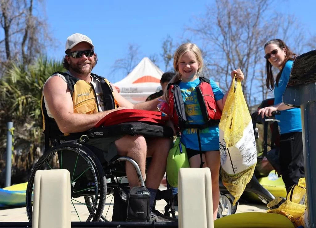 An adult in a wheelchair next to a child, both wearing life jackets