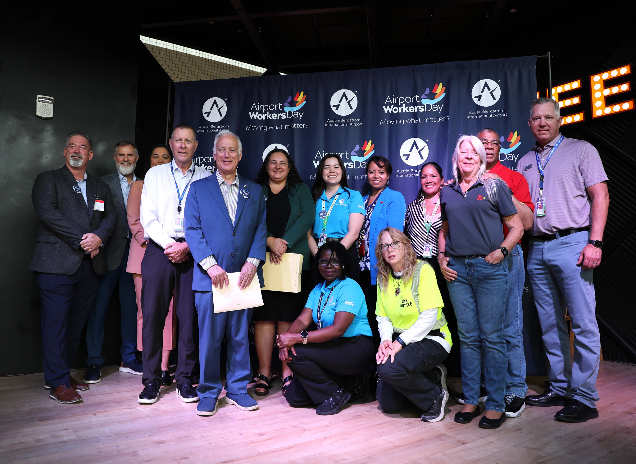 Group photo from the Austin-Bergstrom International Airport Workers Day Proclamation Event at Austin-Bergstrom International Airport on June 25, 2026. Austin Mayor Kirk Watson and AUS CEO Ghizlane Badawi stand in the center of the group, joined by airport