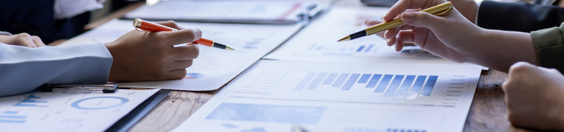 Group of people pointing to graphs and charts on a table.