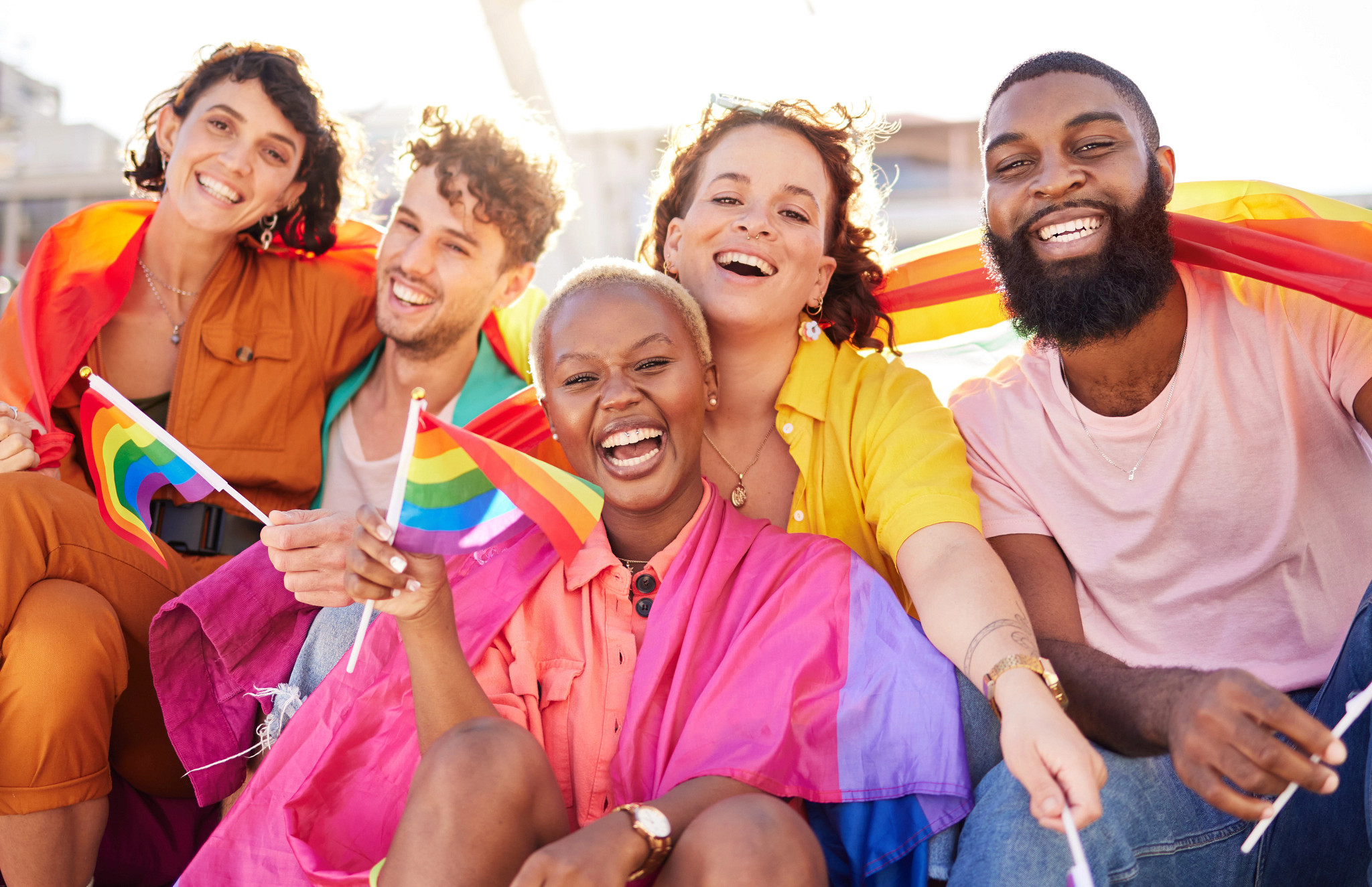 Group of diverse friends smiling together with LGBTQIA+ Pride flags