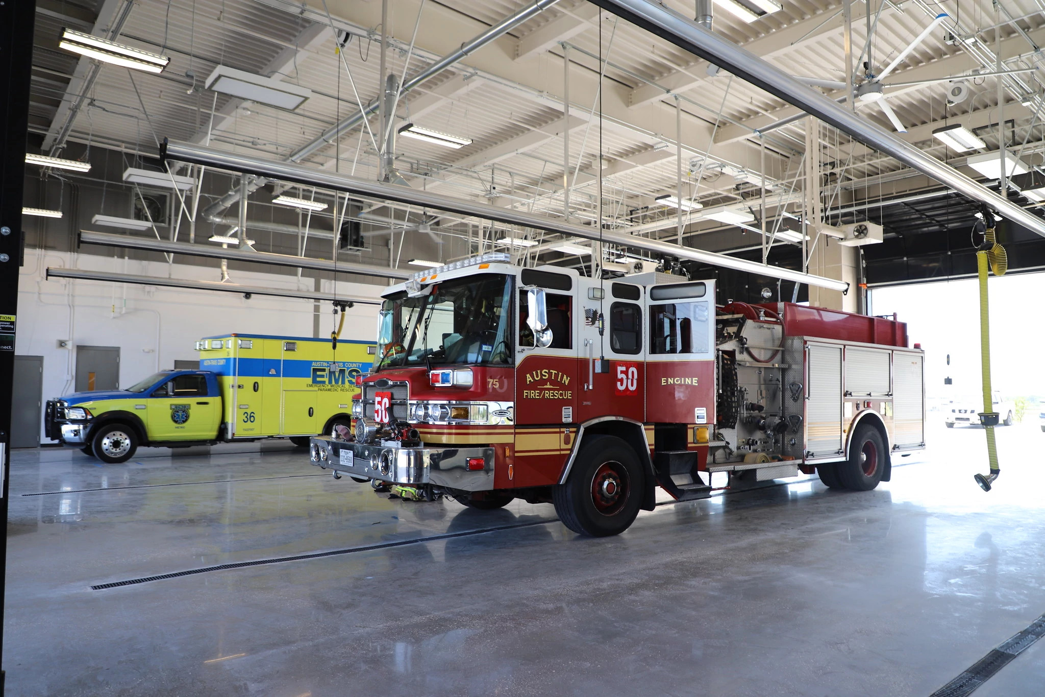 An Austin Fire Department fire engine and Austin-Travis County EMS ambulance are parked inside a shared Fire and EMS station bay.