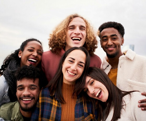 Multiracial and multicultural group of young people smile wide for the camera while embracing each other.