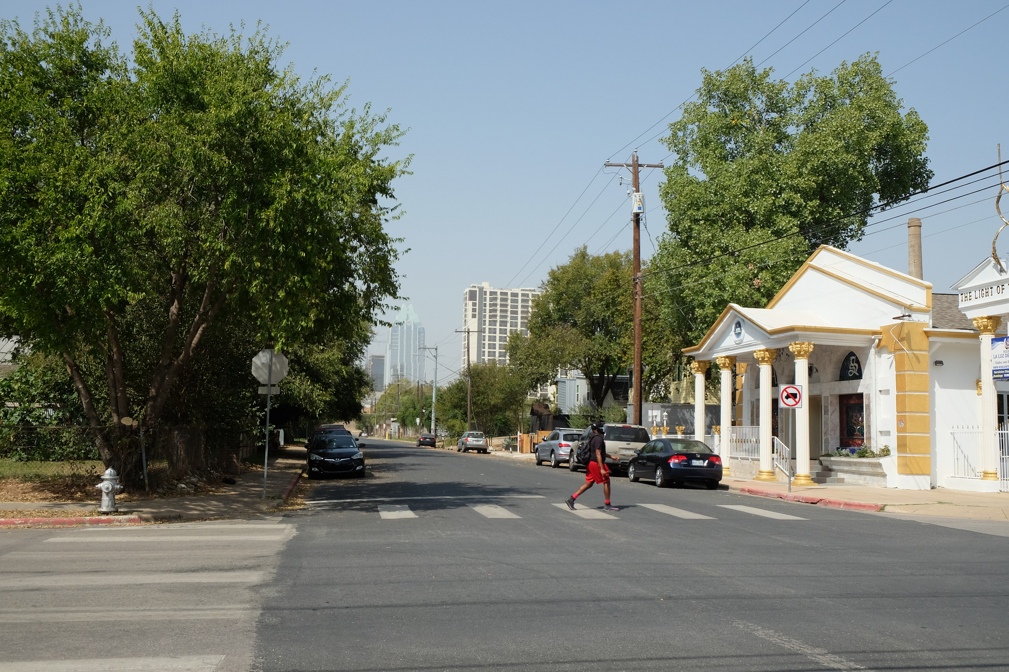 A person crosses a street in east Austin with a hazy sky above. Downtown Austin and I-35 are seen in the background.