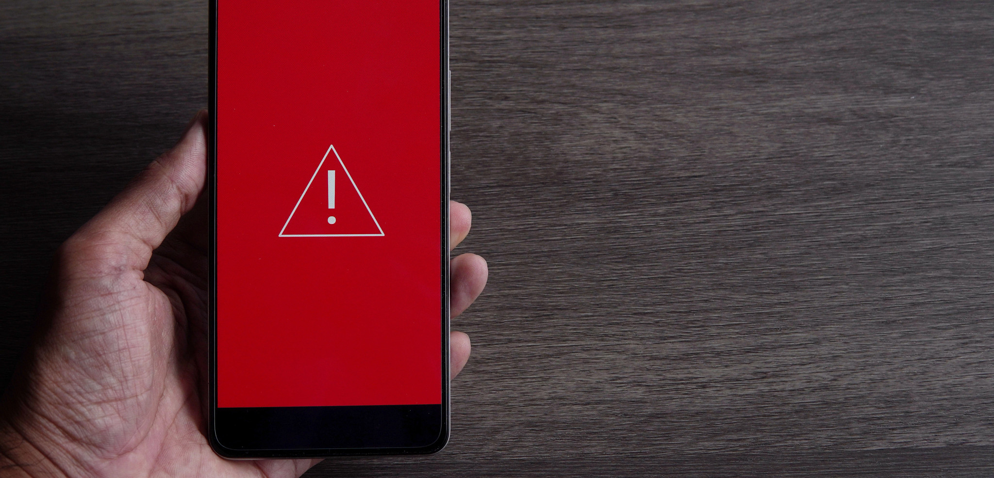 photo of hand holding cell phone with an alert icon on the screen