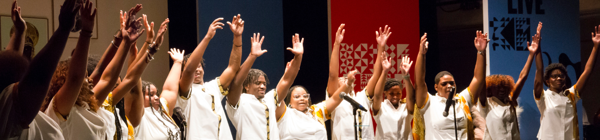 Group of performers raising their hands in celebration on stage at the Carver Museum