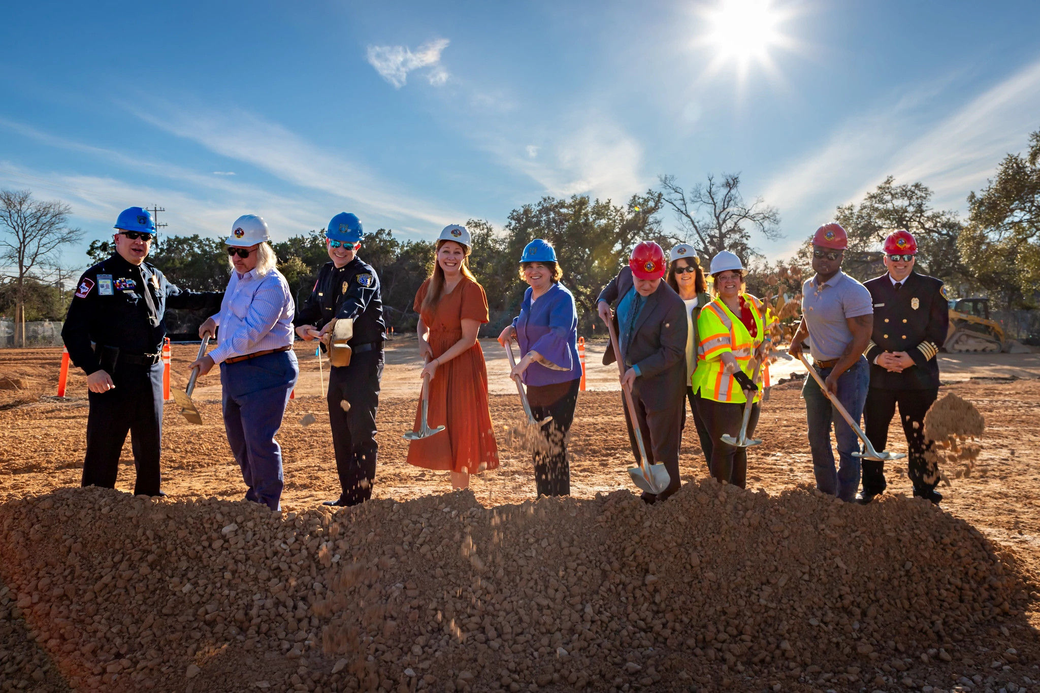 A group of City of Austin staff and public safety officials wearing hard hats use shovels during a ceremonial groundbreaking at a construction site.