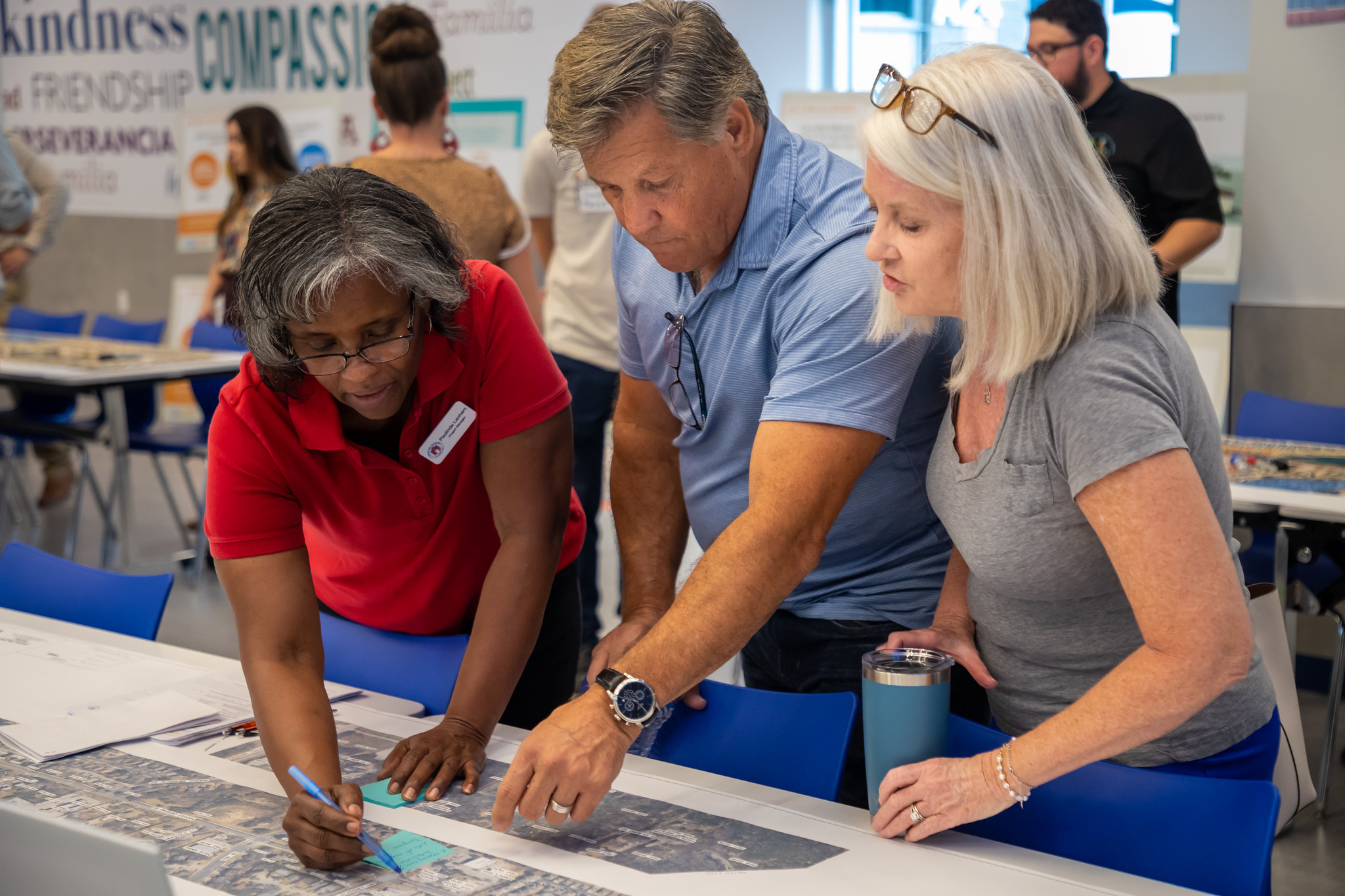 Three people gather around a table, reviewing an aerial map and writing notes during a community engagement event.