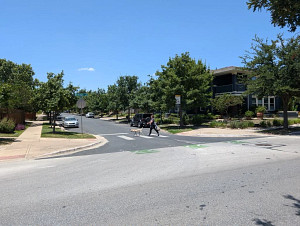 A person and dog cross a street at an intersection that has a shorter crossing distance due to a curb extension.