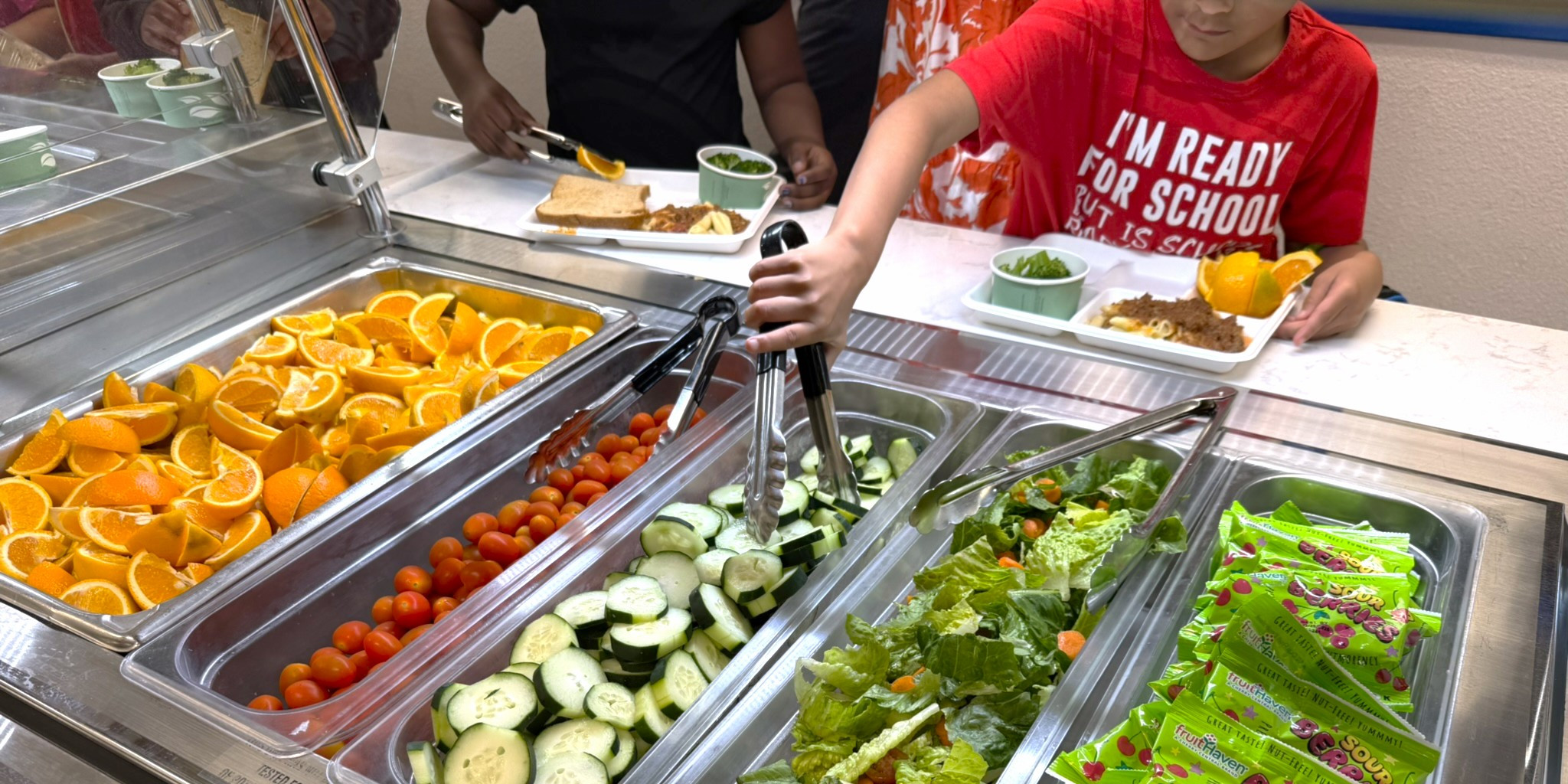 Kids self serving vegetables in the school cafeteria line.