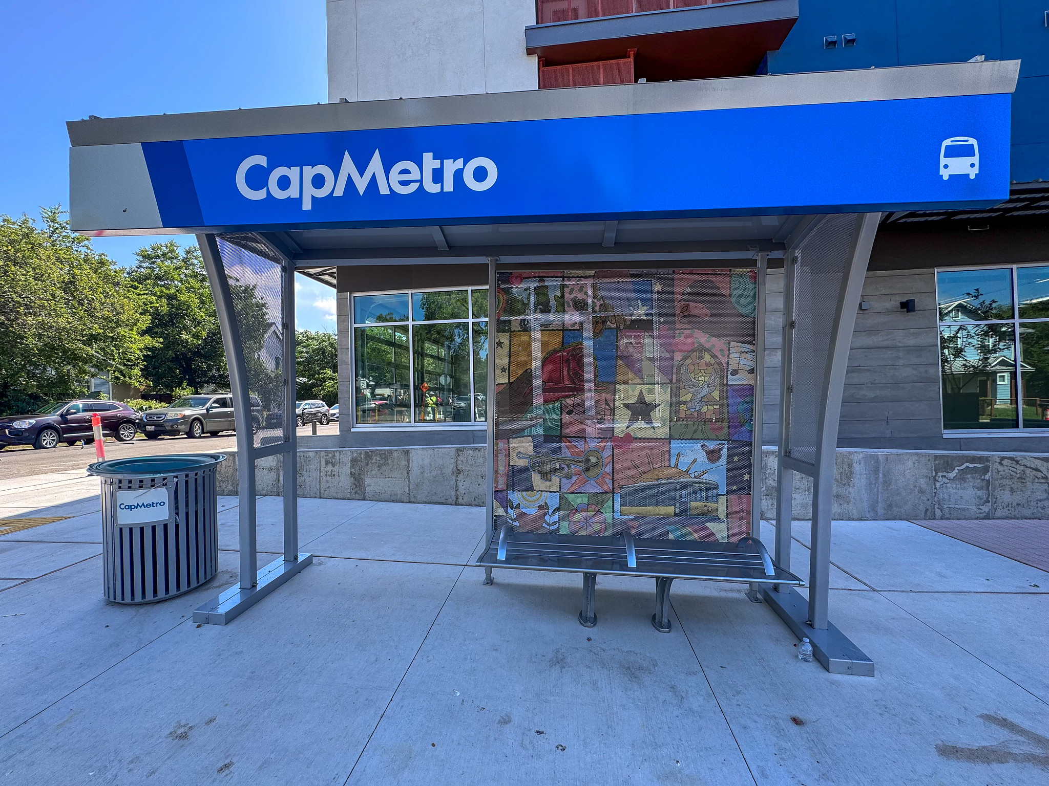 Covered CapMetro bus stop outside The Ivory featuring colorful community artwork inspired by Ms. Scottie Ivory and seating for transit riders.