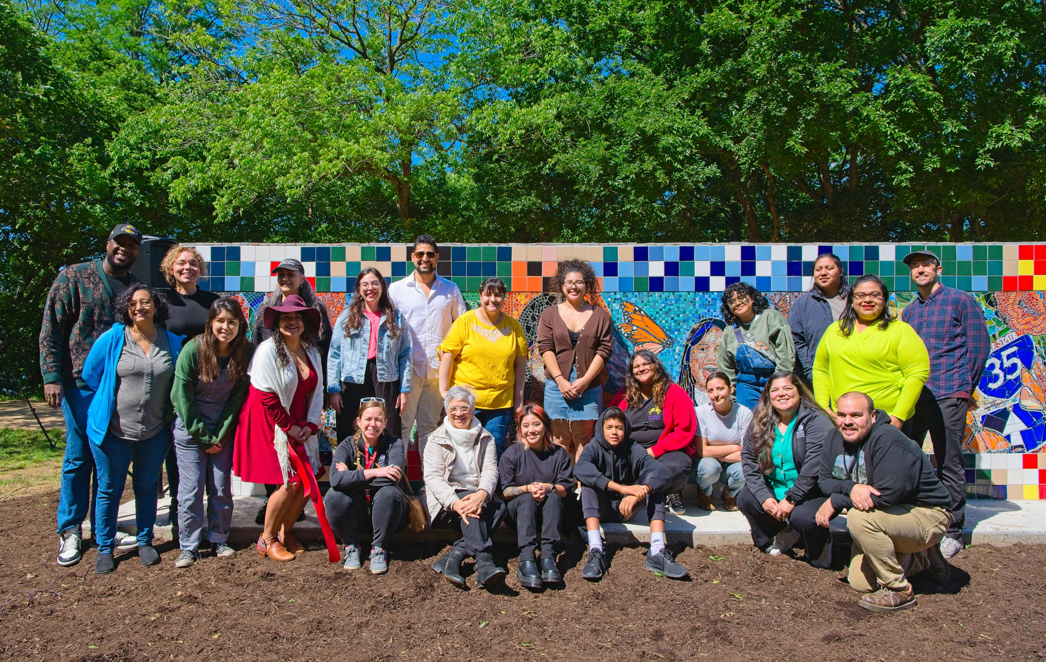Group of people standing in front of a mosaic mural depicting portraits of women
