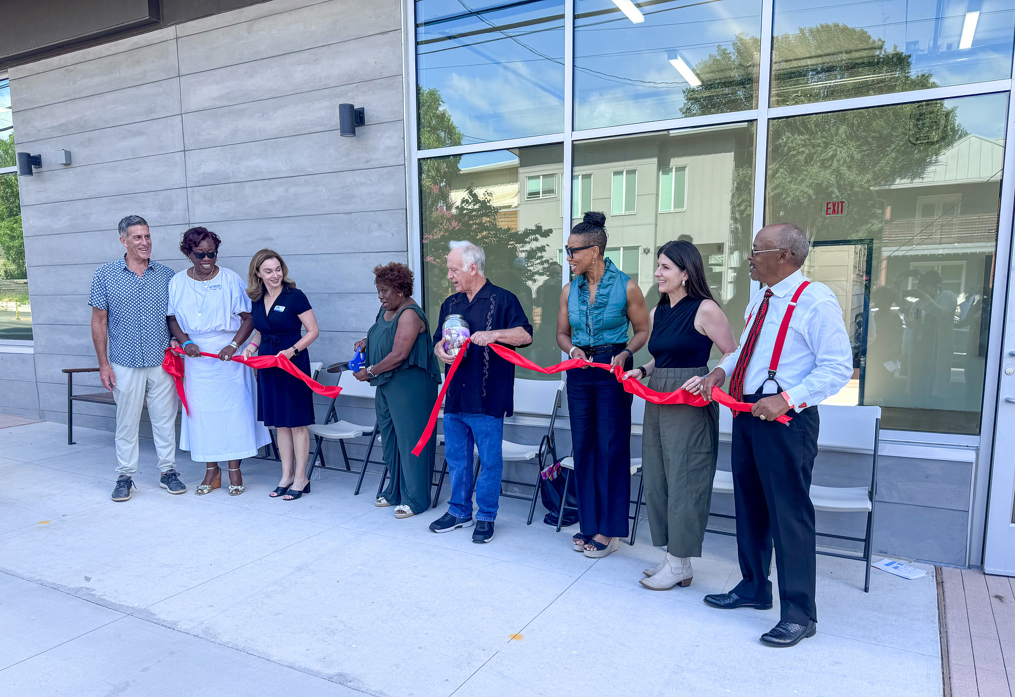 Community leaders and partners hold a red ribbon during The Ivory's grand opening celebration outside the new mixed-use condominium building in Austin.