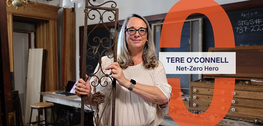 Tere smiles while holding a decorative metal fixture in the Save the Good Stuff shop. A graphic reads, Net-Zero Hero: Tere O'Connell.