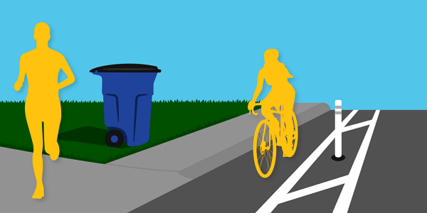 A person jogging on a sidewalk corner. A trash cart is placed on the lawn, close to the sidewalk. A cyclist rides a bicycle in the bike lane.