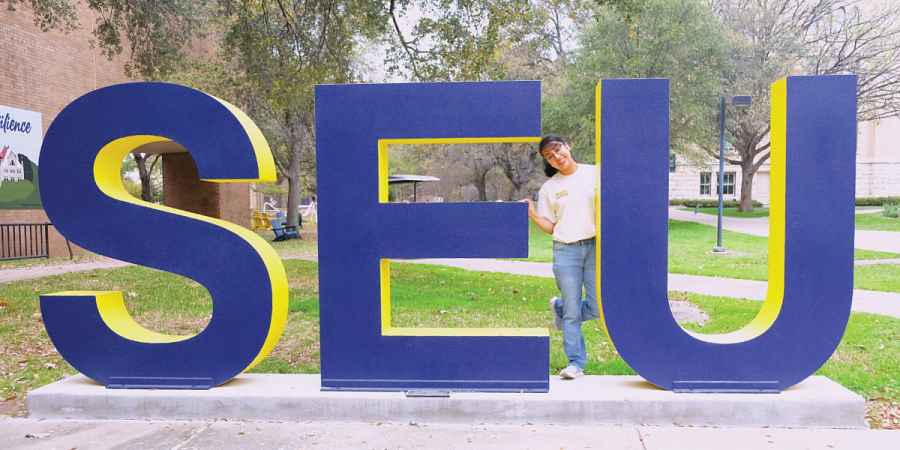 Emily Hernandez-Corona smiles standing between the S-E-U letters at St. Ed's campus.