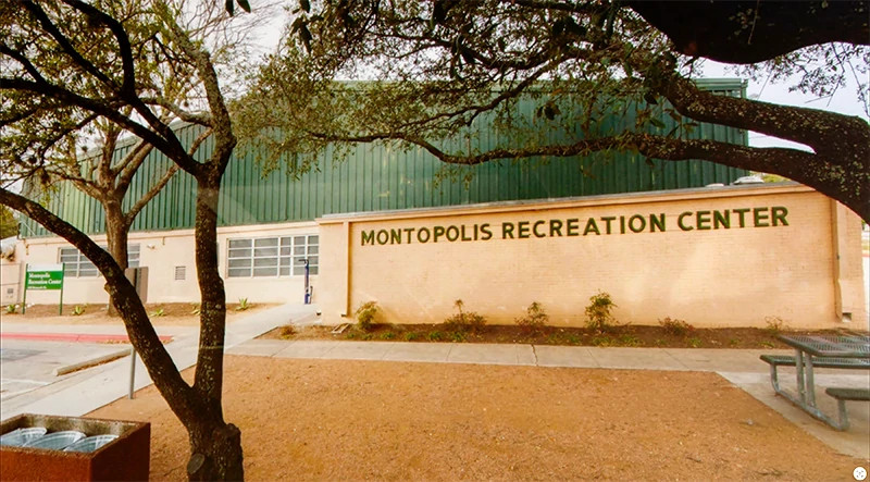 Exterior of the former Montopolis Recreation Center, a beige brick building with green siding, viewed through large trees.