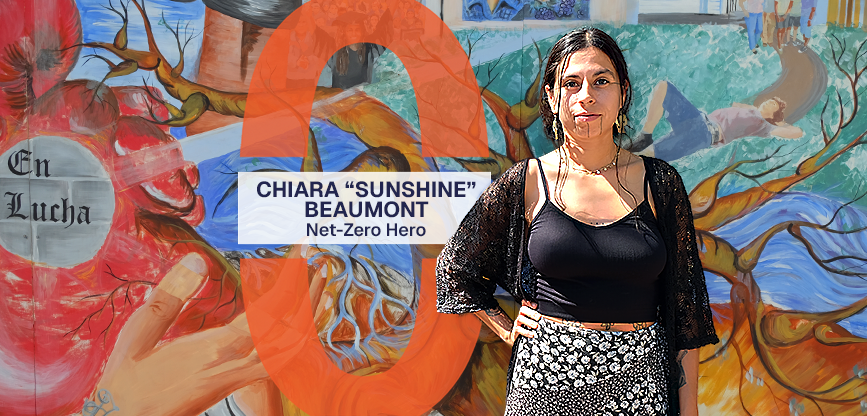 Chiara Sunshine Beaumont stands in front of a mural at Red Salmon Arts. Text reads, Chiara Sunshine Beaumont, Net-Zero Hero.