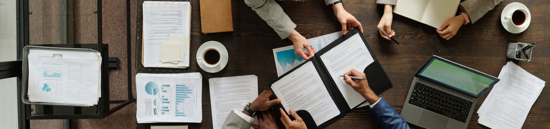 Banner with overhead view of business people signing a contract on a cluttered table