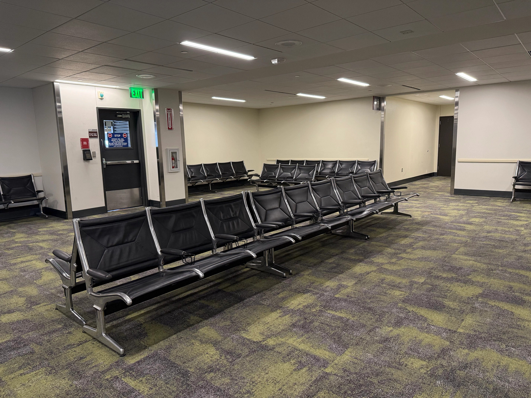 A picture of the AUS gate 13 hold room area. There are chairs in the middle of the room and chairs against the wall.