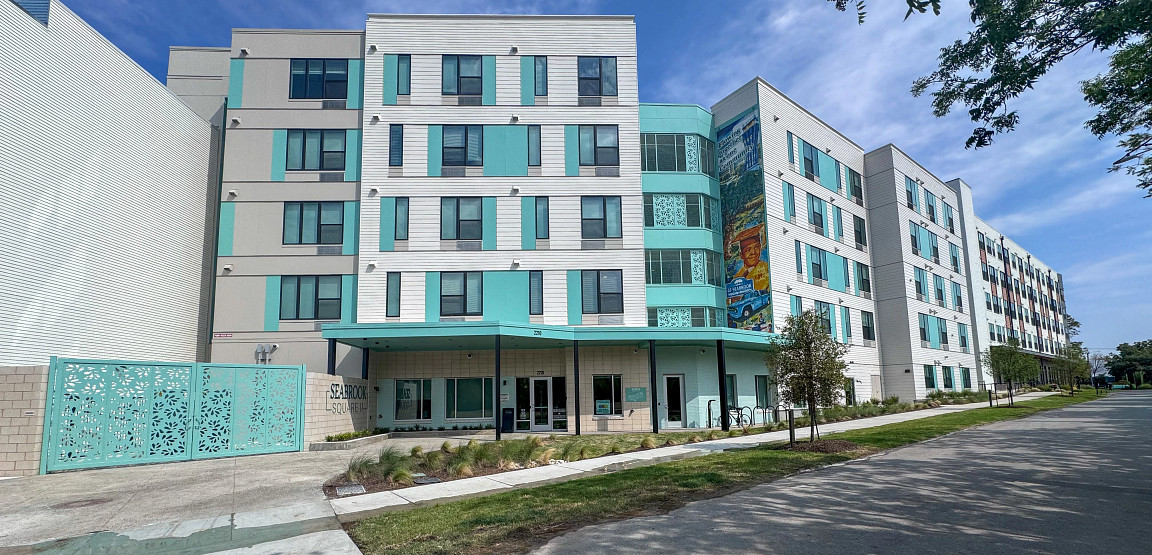 Exterior view of Seabrook Square II, a PSH community in East Austin, with a decorative gate, mural, and landscaped walkway.