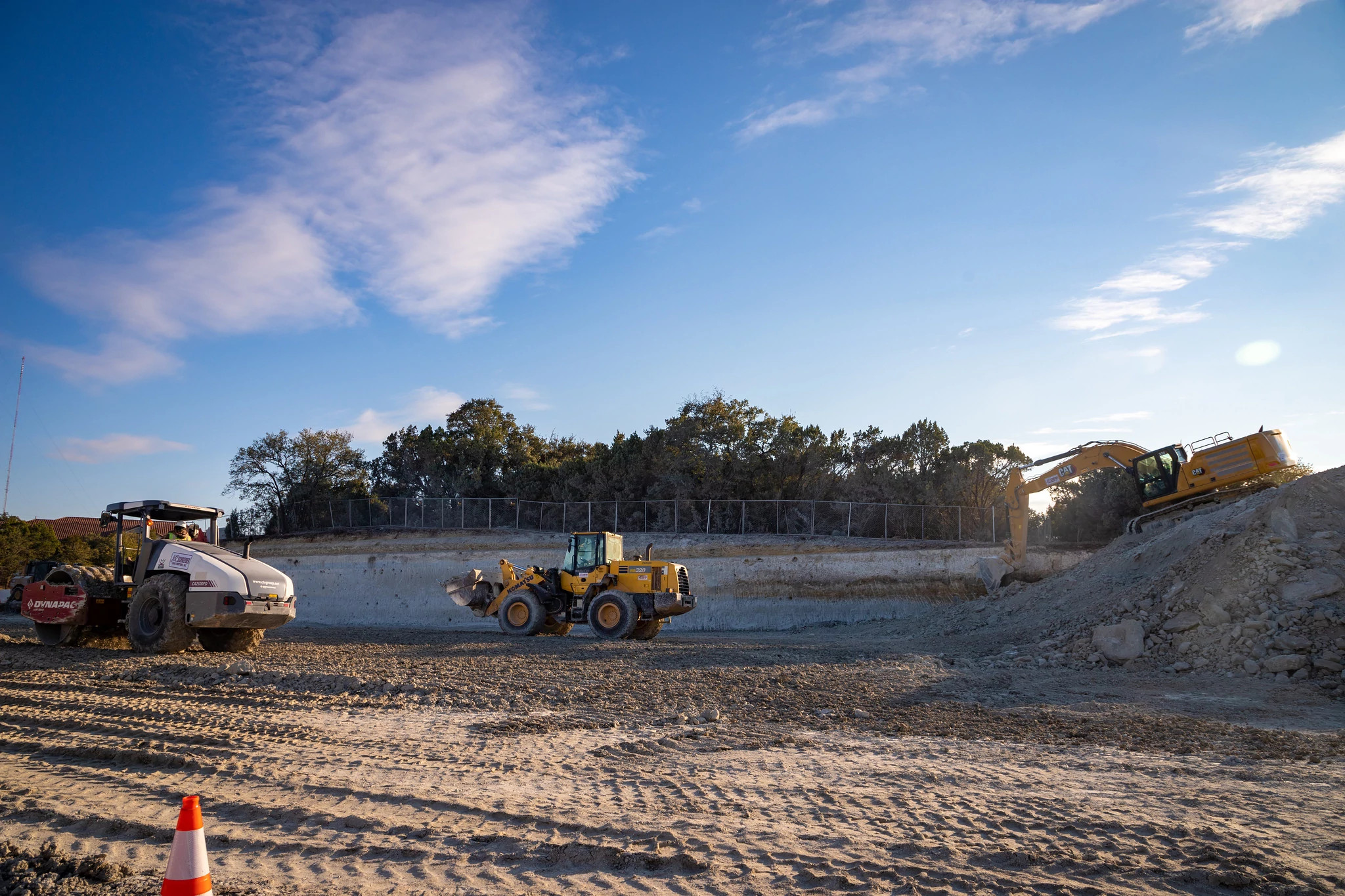 Construction equipment, including a roller, front-end loader and excavator, works at an excavated construction site.