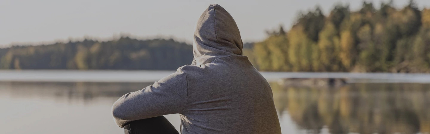 man in a hoodie looking over a lake