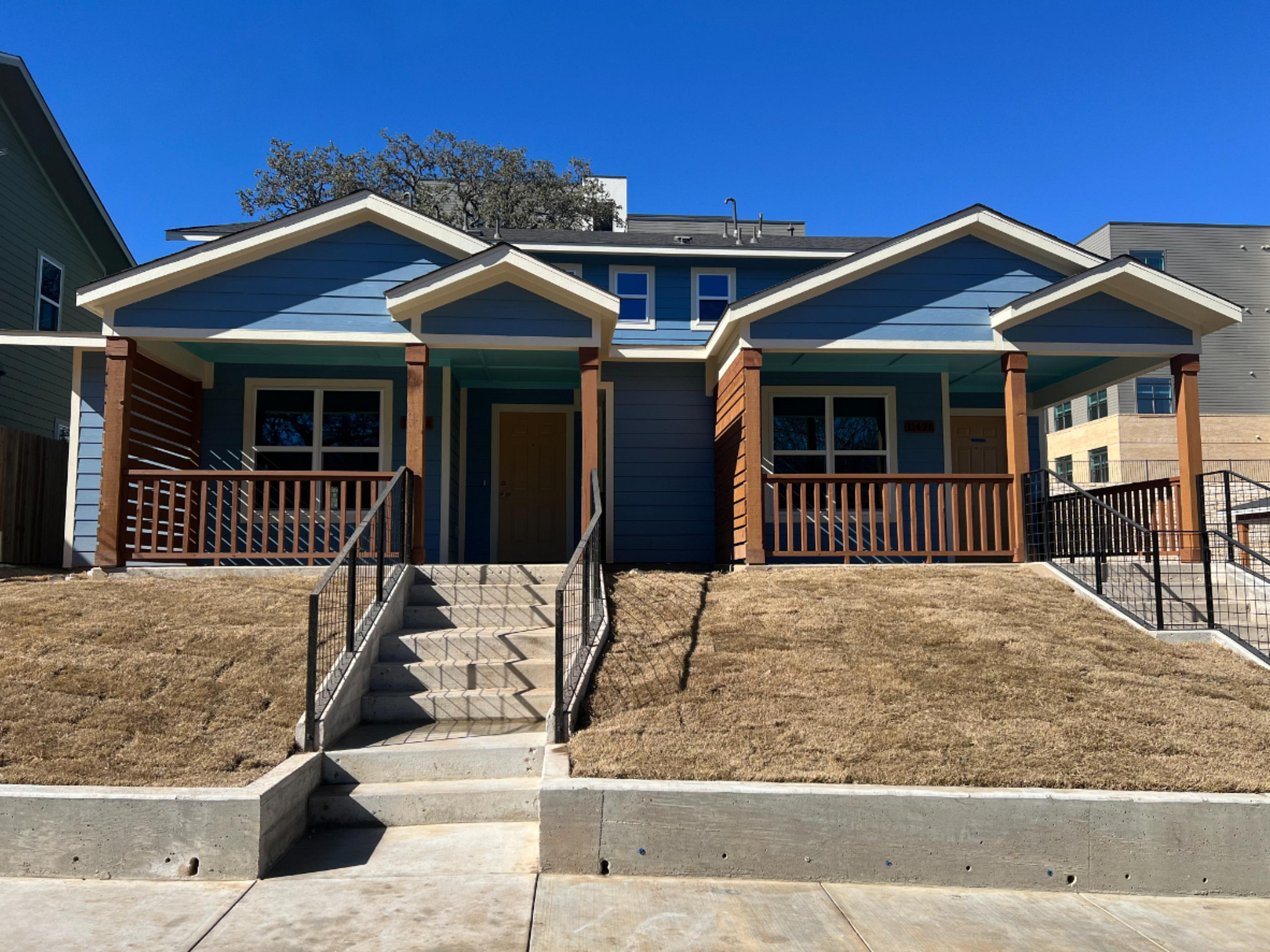 Image a two-story duplex with two townhomes. The exterior is blue with brown wood railings and columns on the covered front porch.