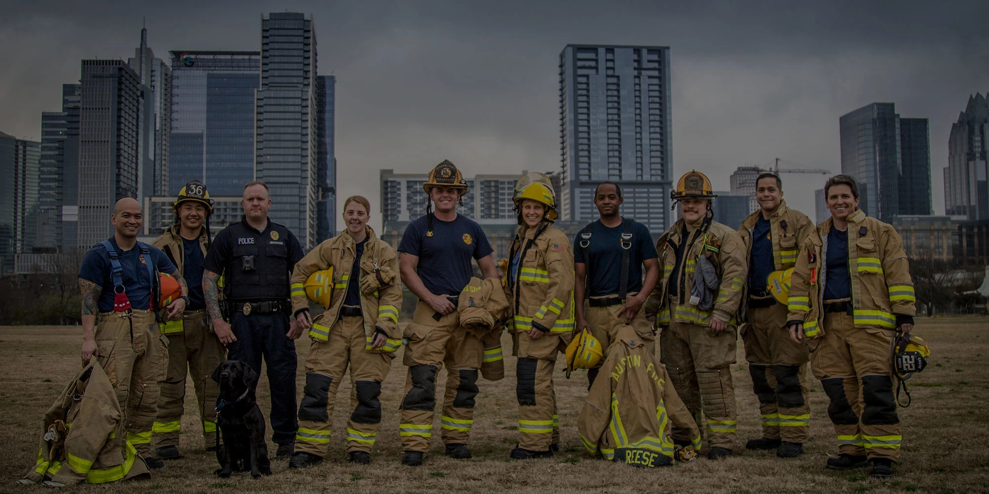 Ten firefighters standing in front of downtown Austin buildings in uniform 