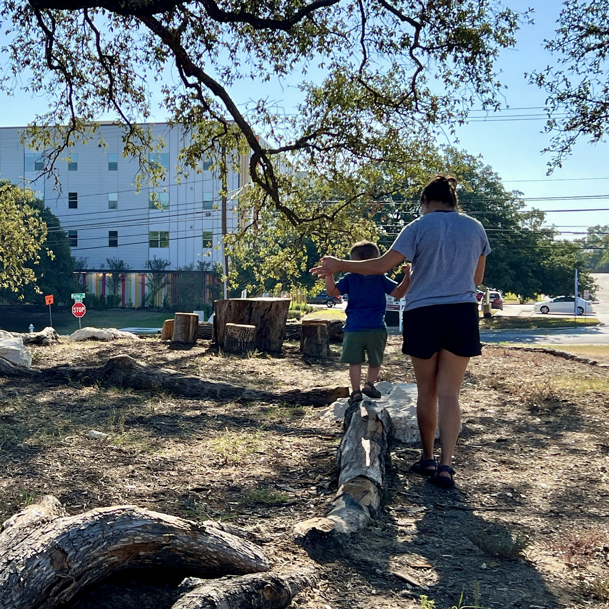 A parent helps a toddler walk across a balance log