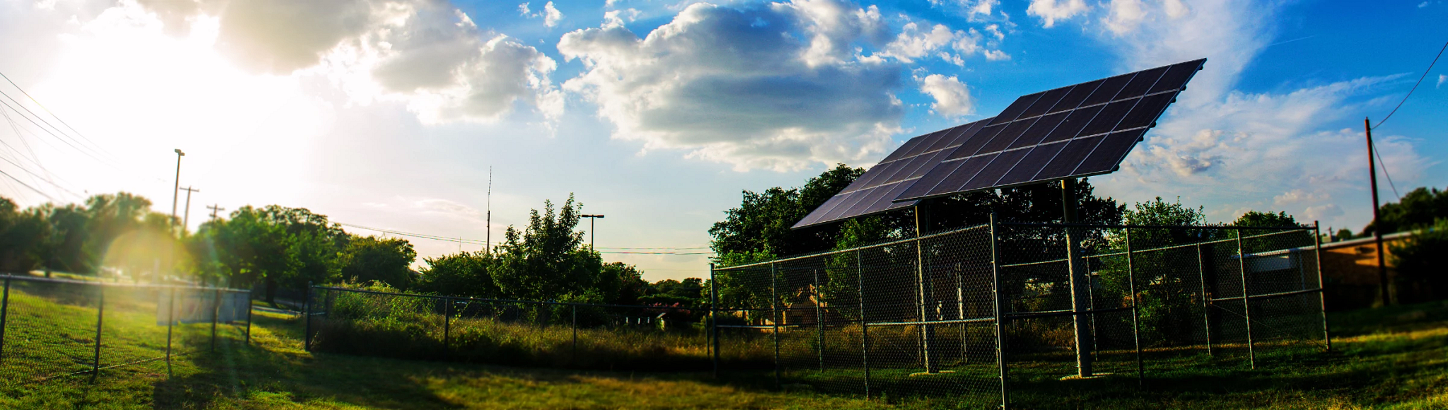A set of solar panels in a field in Austin with power lines in the background.