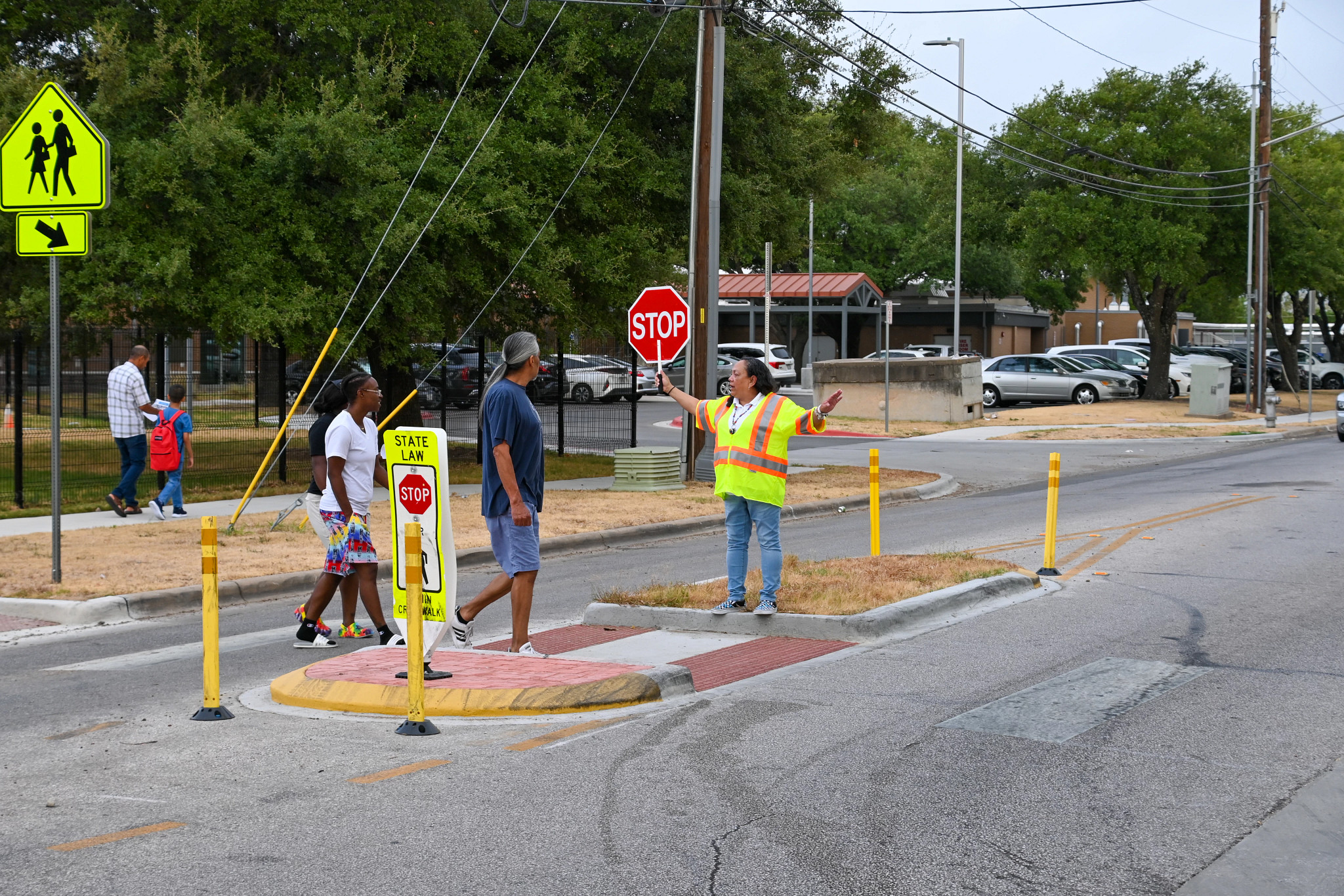 Crossing guard holds stop sign as parents and students cross the street near a school.