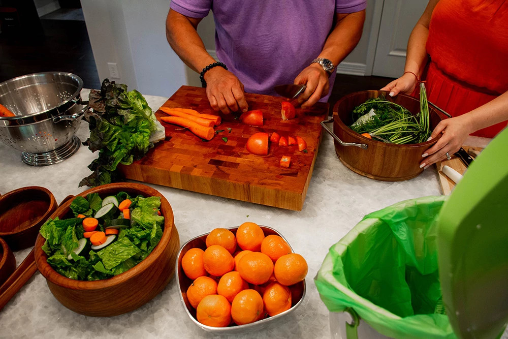 A family prepares food on the kitchen counter, the cut pieces are set aside for composting.