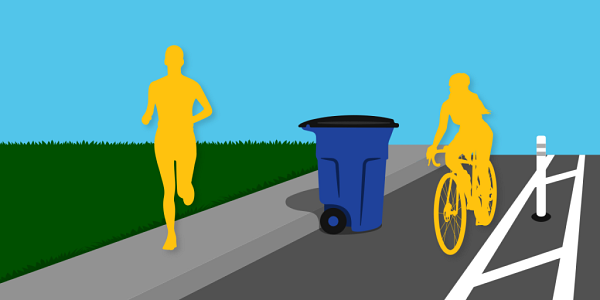 A person jogging on a sidewalk, a recycling cart in a bike lane close to the curb, and a cyclist riding a bike in the bike lane.