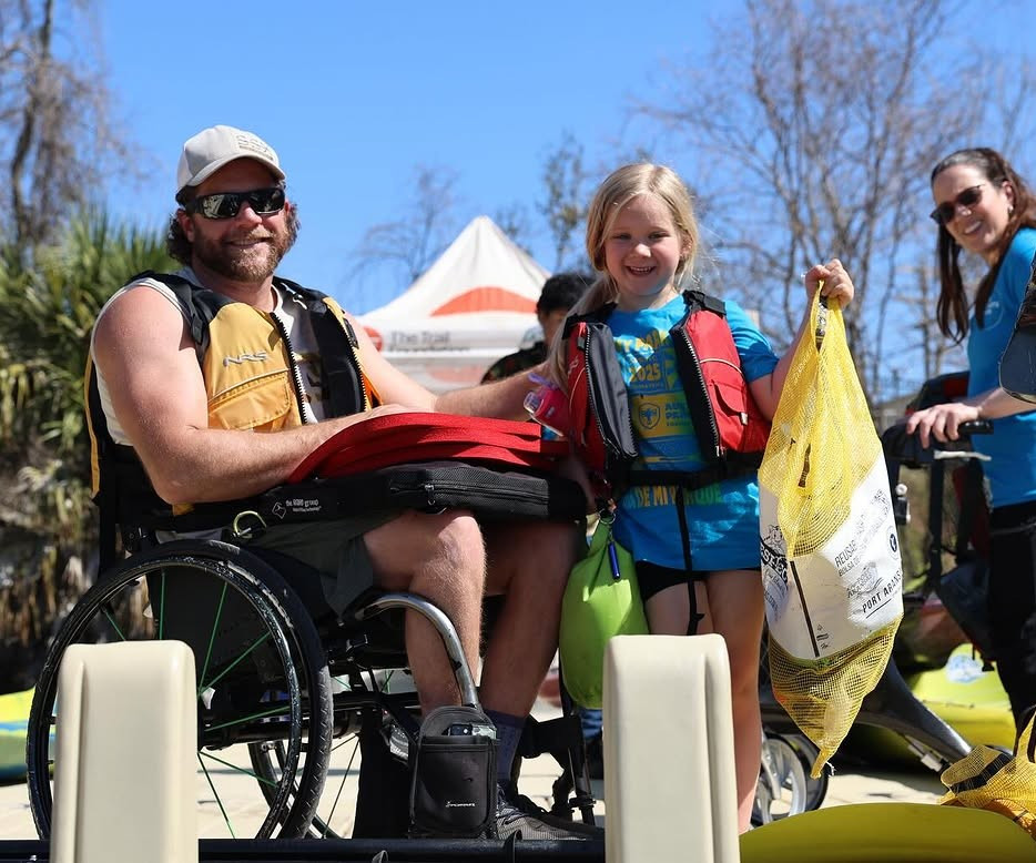 An adult in lifejacket in a wheelchair and a child in a lifejacket pose with a bag of litter