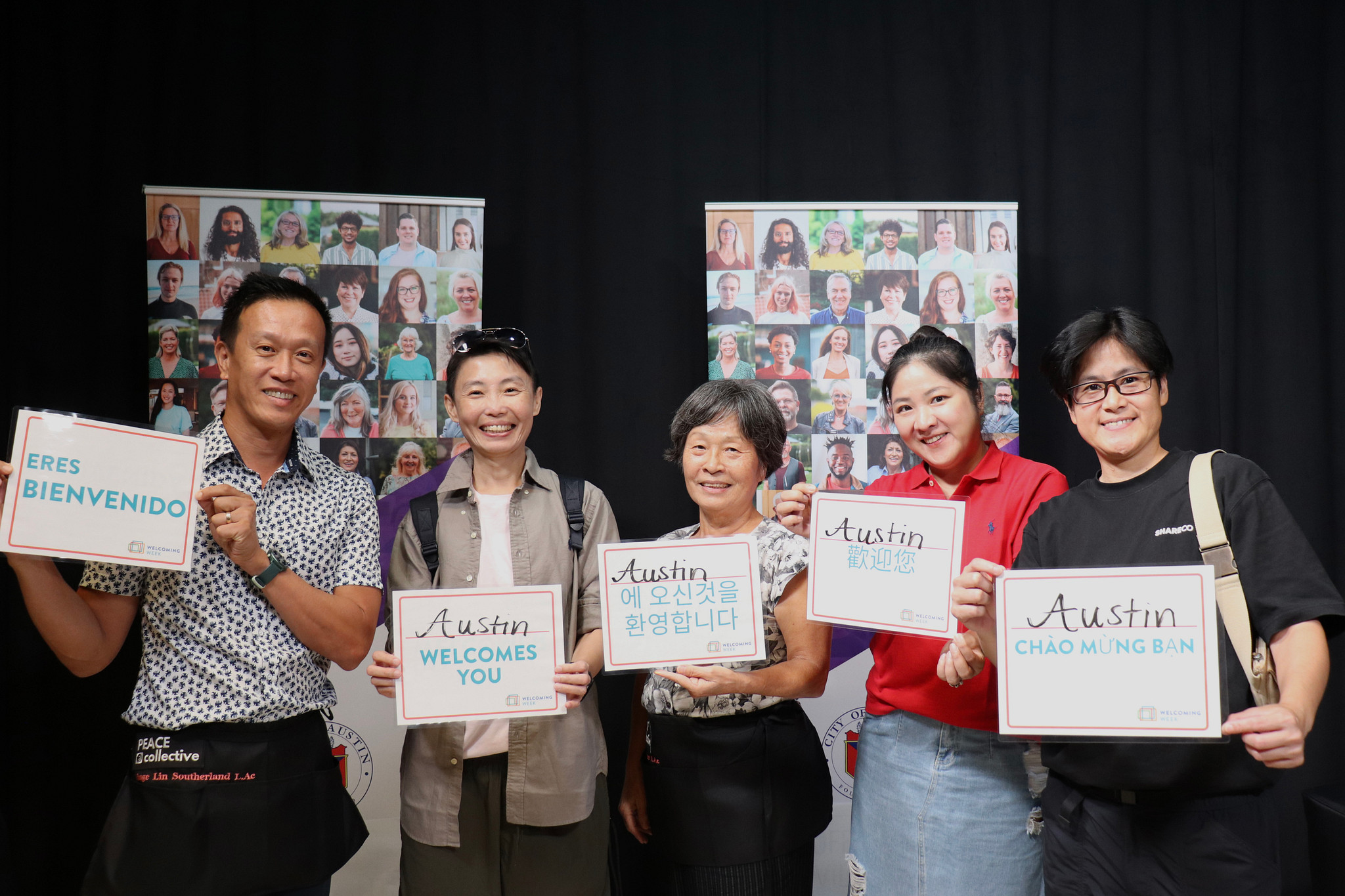 Truc Viet, a group of Asian acupuncturists, pose with 'Austin Welcomes You' signs in multiple languages at the 2025 inaugural Welcoming Week kickoff at Austin City Hall