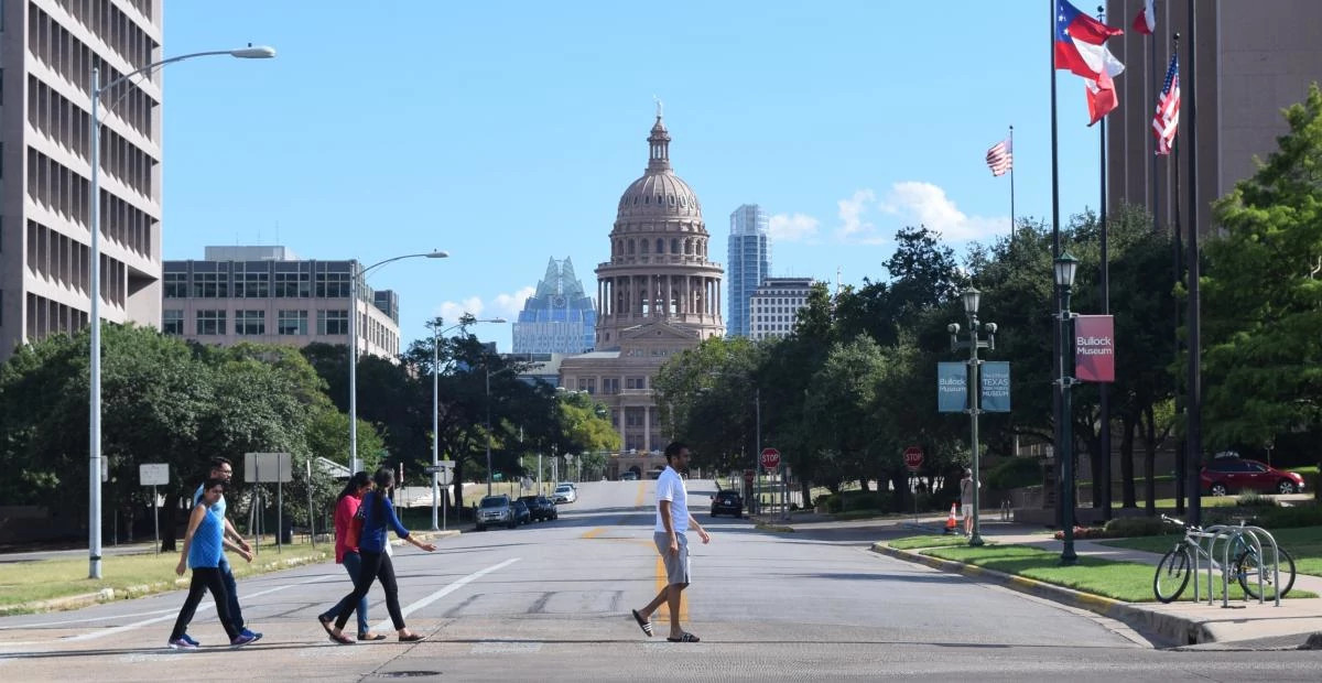 People cross the street in the shadow of the Texas state capitol.