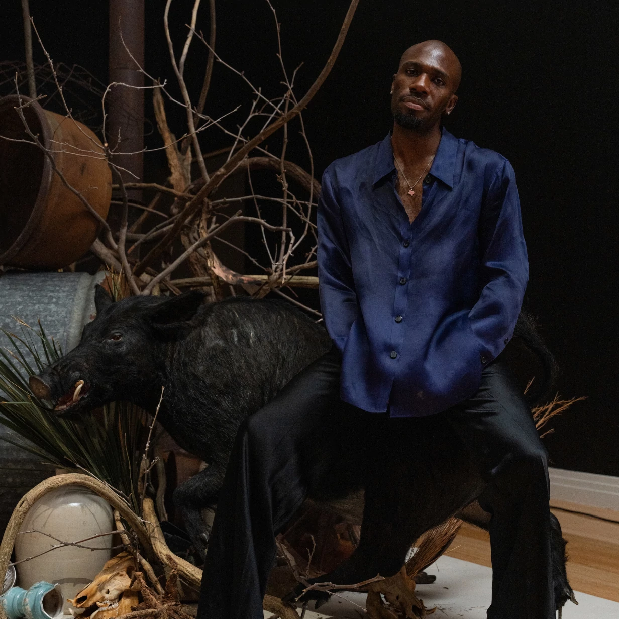 Texas-based artist Hakeem Adewumi seated in front of his artwork at the George Washington Carver Museum