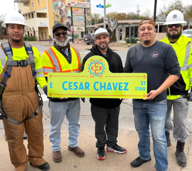 five individuals stand with a street sign for East Cesar Chavez Street
