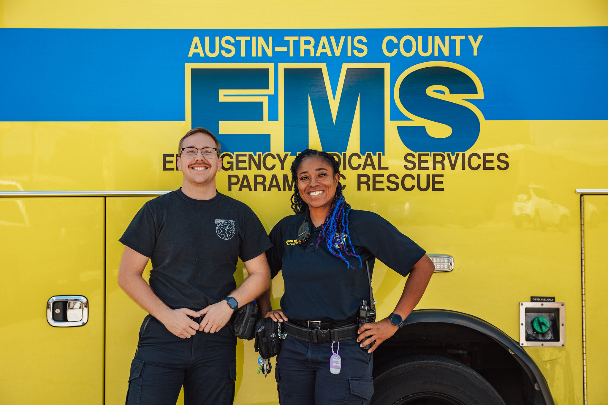Two smiling EMTs in front of an ambulance