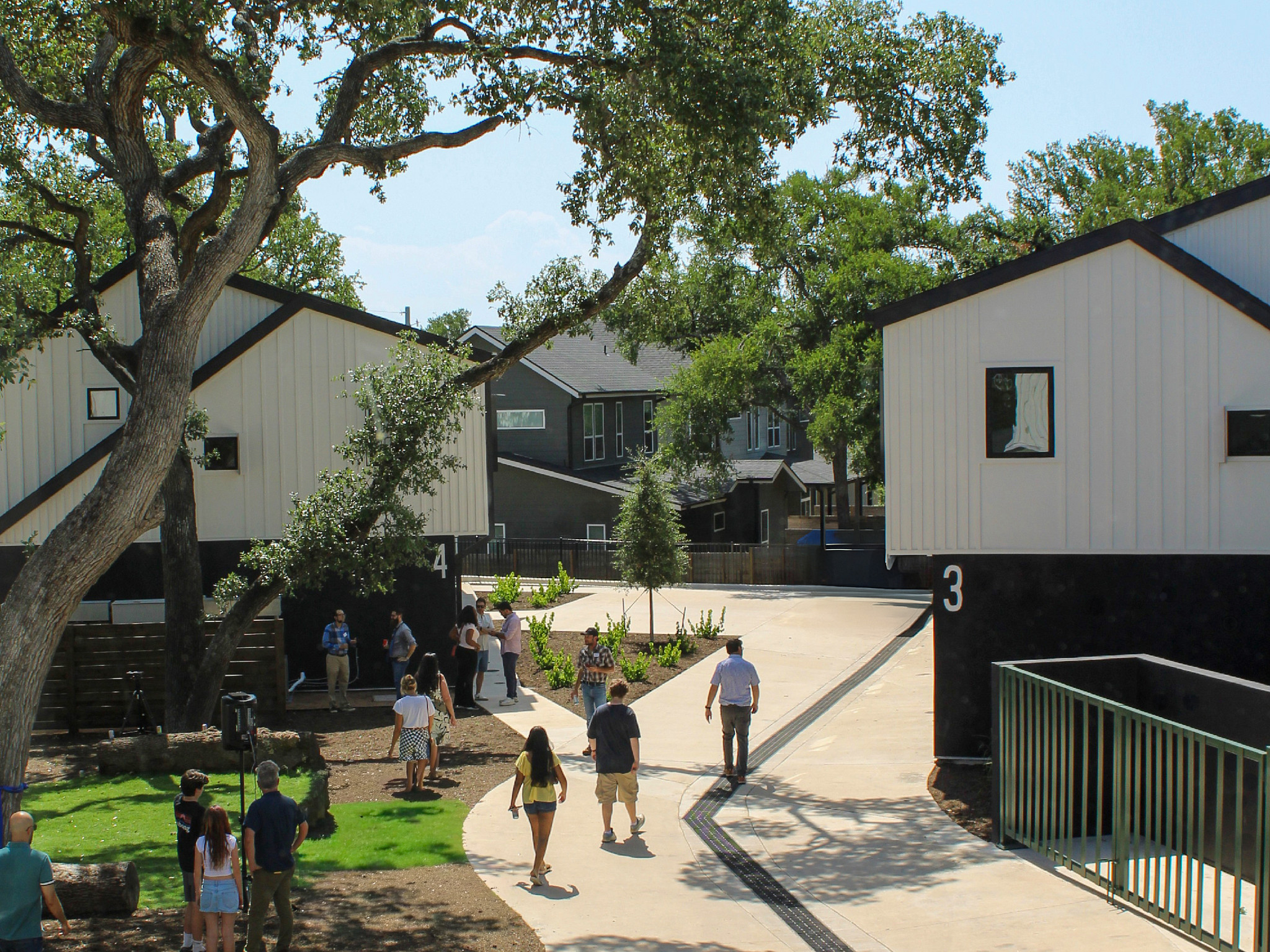 a group of people walking into a new townhome community surrounded by big green trees