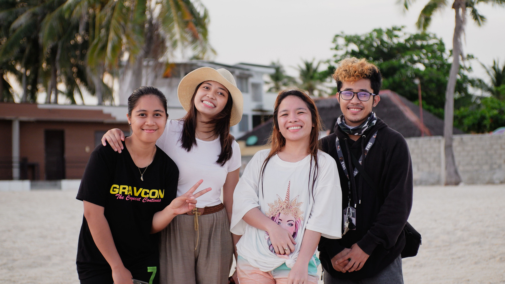 Group of friends of Asian descent pose for a group photo with palm trees in the background.