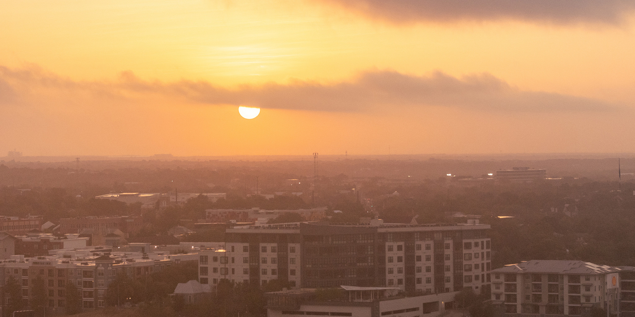 Bright orange sky with hot sun over a cityscape.