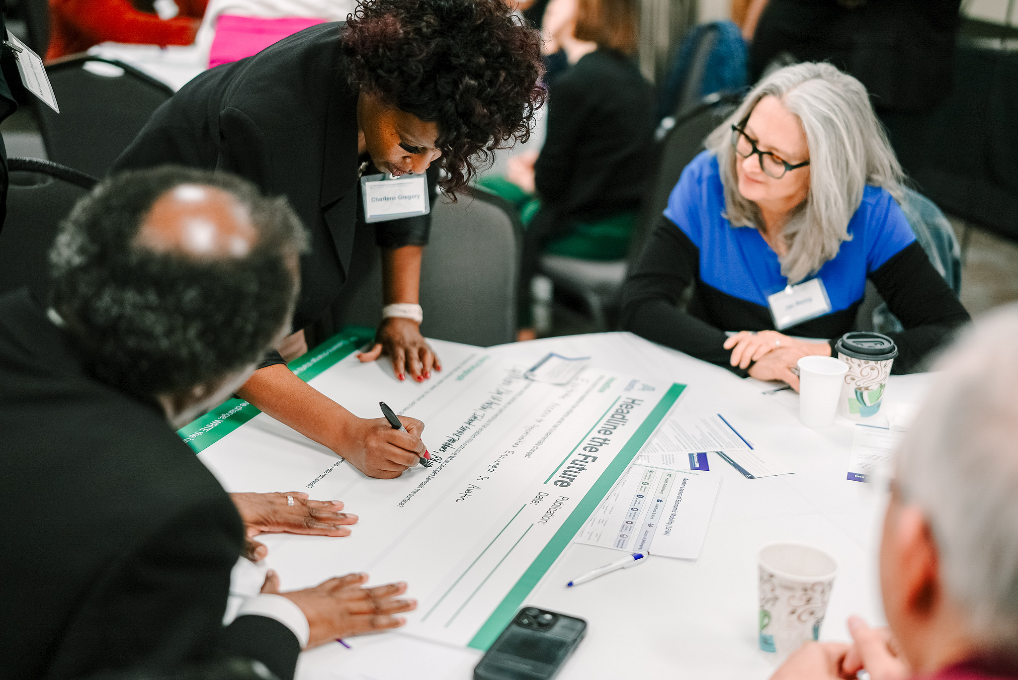 A Black man, Black woman, and white woman work in a group together to write ideas on chart paper at a conference.