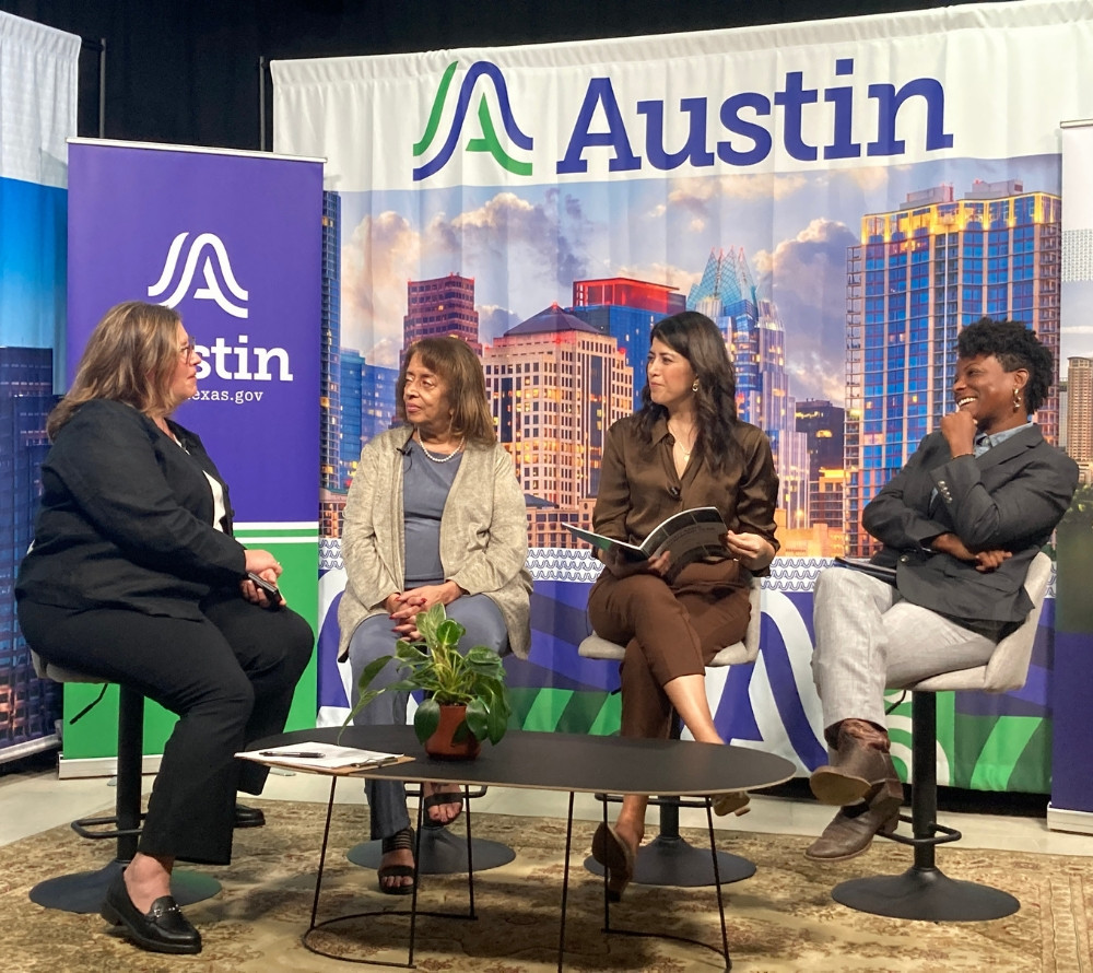 A photo of a host talking to three guests on a talk show panel.