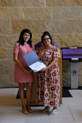 Councilmember Vanessa Fuentes presents a Certificate of Participation to a representative of the Refugee Collective in front of the podium at City Hall Welcoming Week Kickoff event in 2025